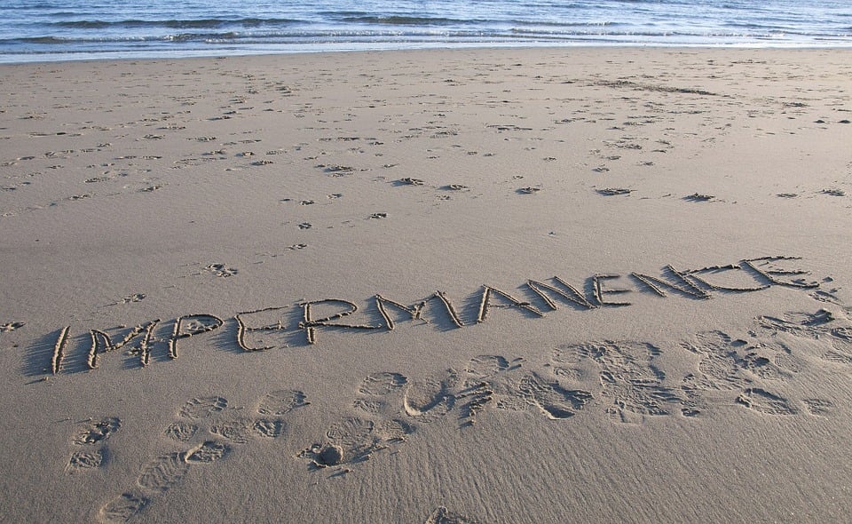The word impermanence written on a sandy beach