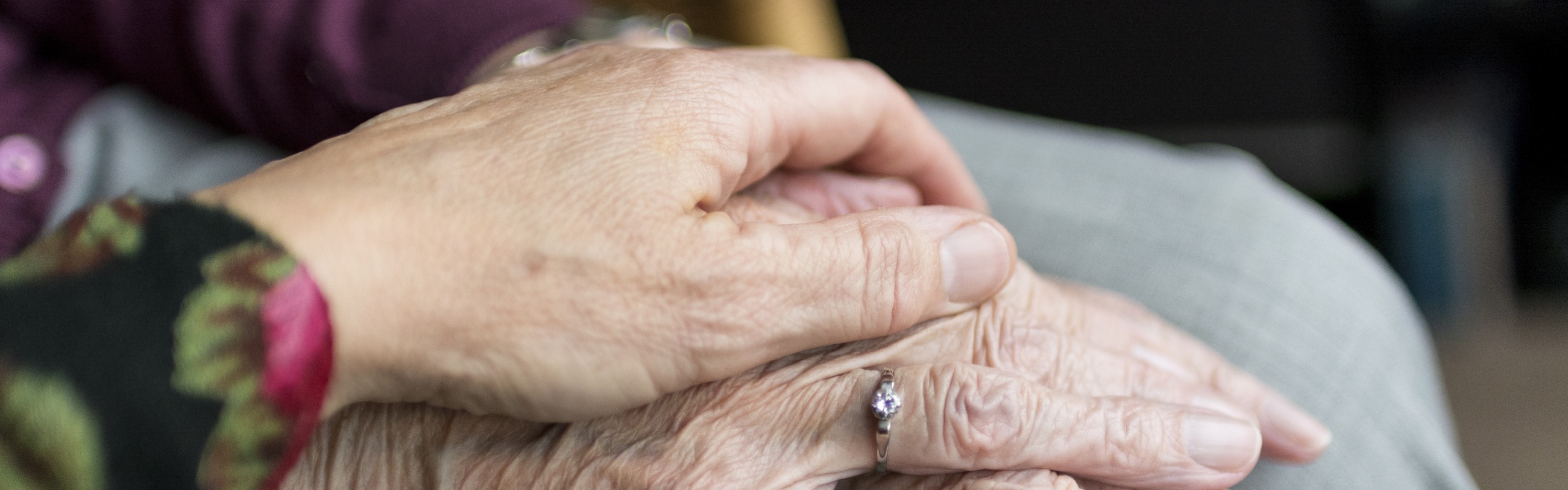 A hand lays on top of another, wrinkled hand