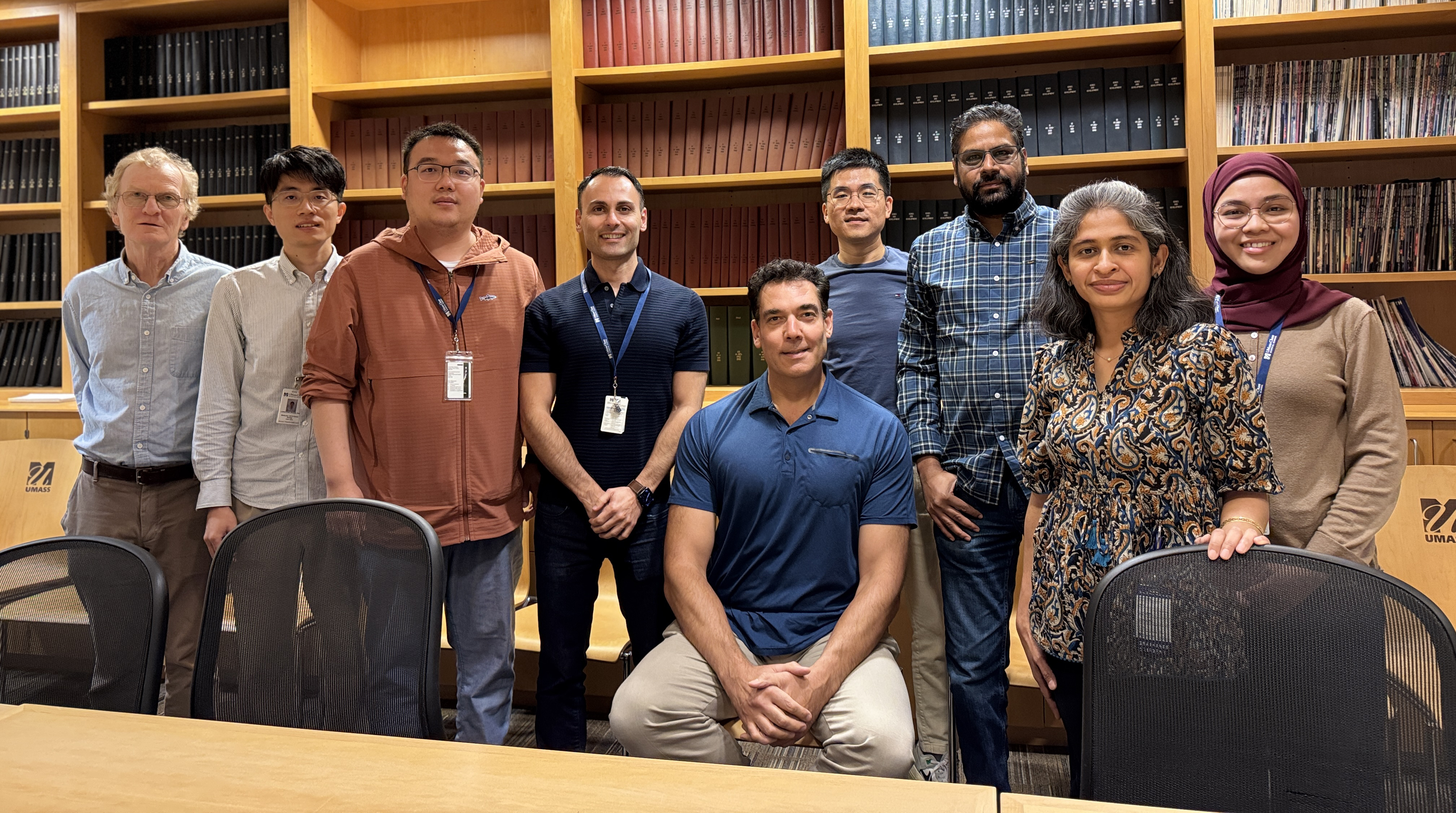 Group photo of the Gregory Lab in a conference room. Richard Gregory is seated at the center, surrounded by eight lab members, standing and smiling at the camera.