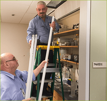 The image shows two people in a room replacing a light bulb