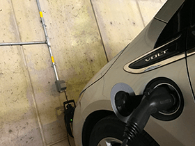 Image shows a close up of an electric vehicle charging port with a cable in it, indicating the car is charging