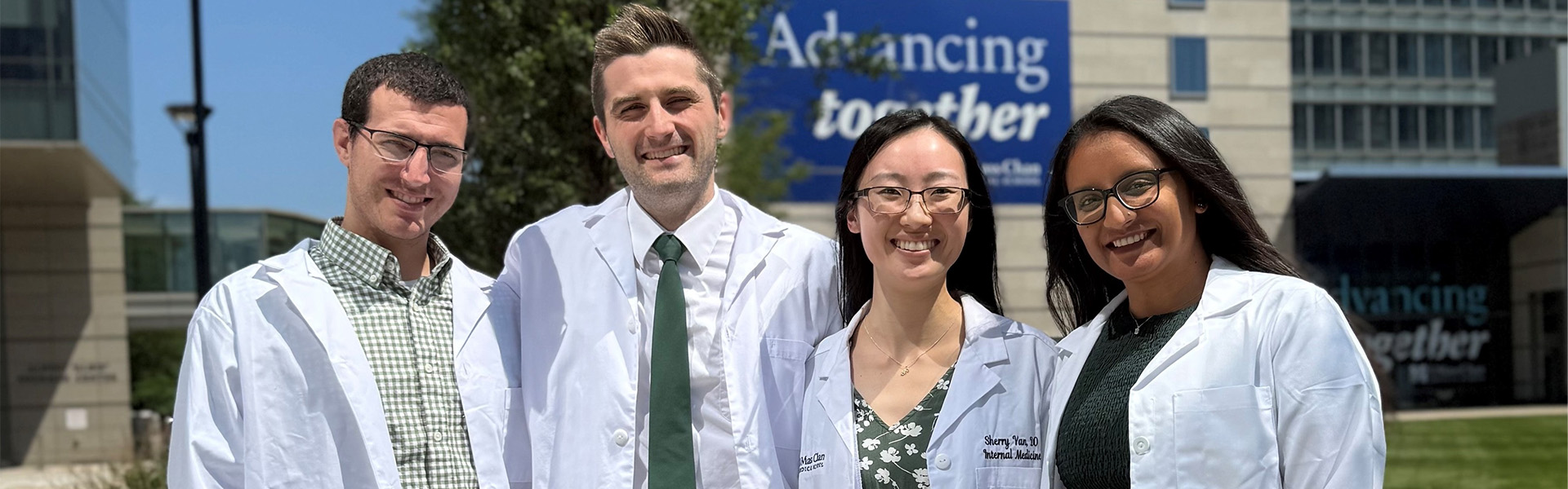 Image of four Primary Care Residents standing in front of the UMass Chan Medical School building