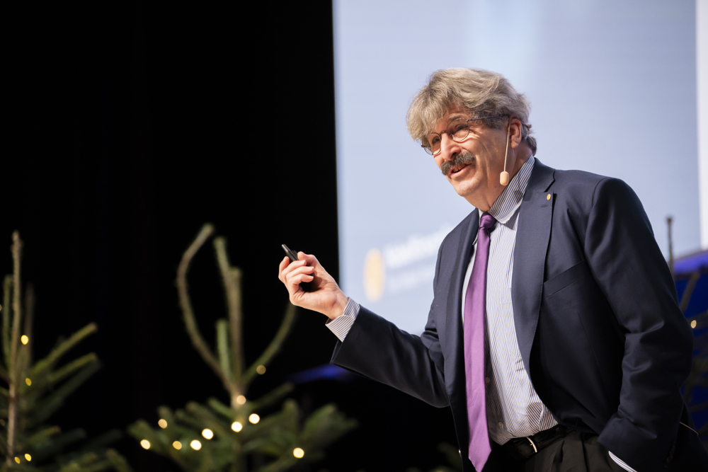 Gary Ruvkun delivering his Nobel Lecture in Stockholm wearing a dark shirt and purple necktie