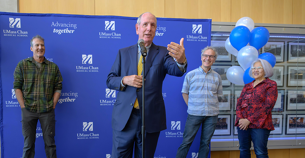 Chancellor Collins speaking at a campus Nobel celebration in October. He shares the stage with Craig Mello, Victor Ambros and Rosalind Lee. Their is a UMass Chan banner in the background and Collins is speaking into a microphone. 