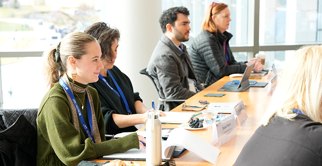 Participants sitting at a long table in front of bright windows